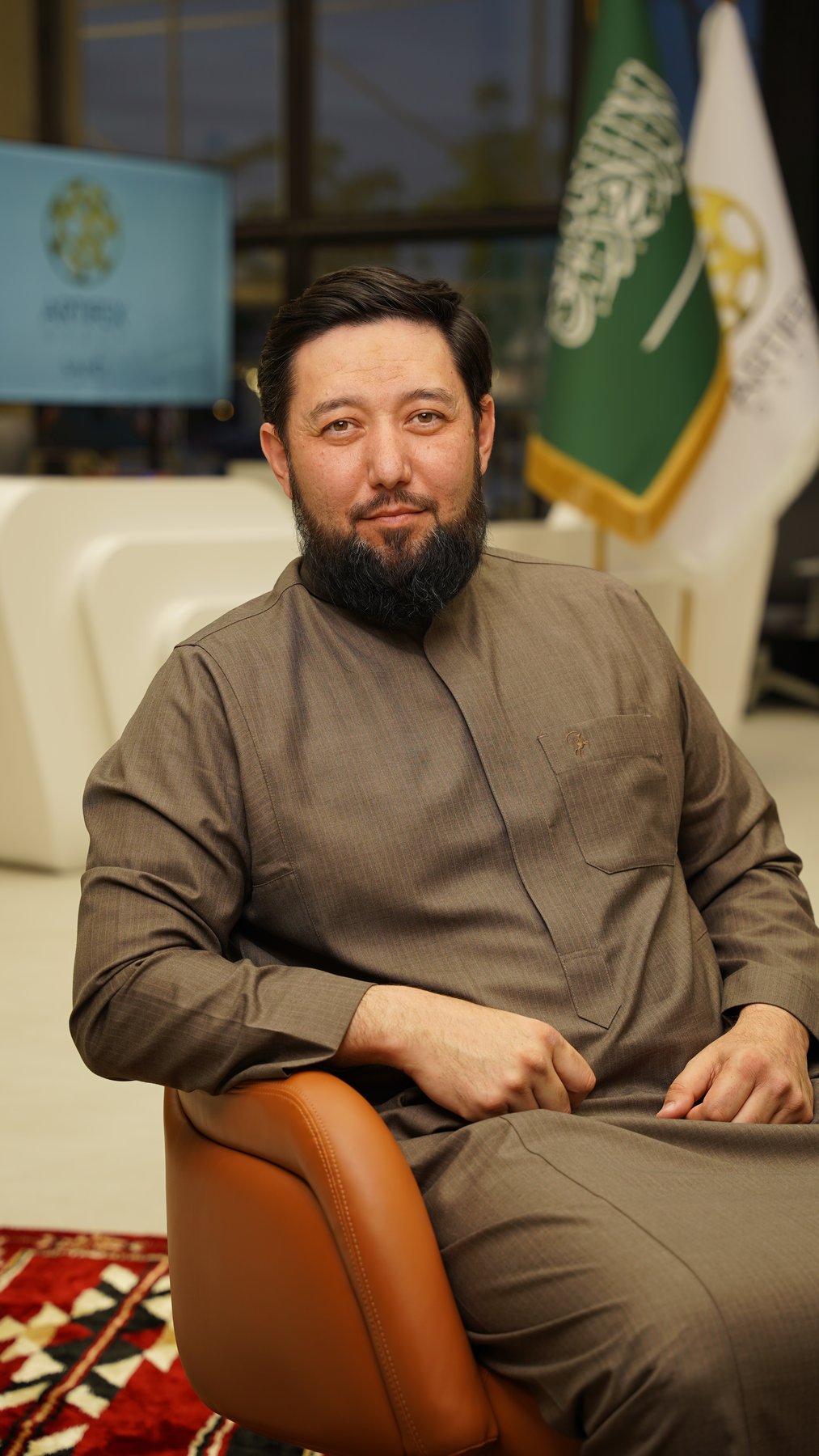 Rustam Khaitmetov at the desk beside the Saudi flag